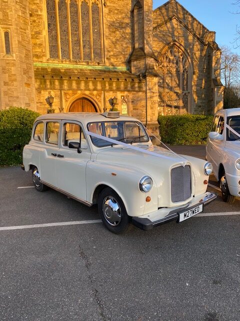 Classic Fairway wedding taxi dressed with ivory ribbons outside a stone church